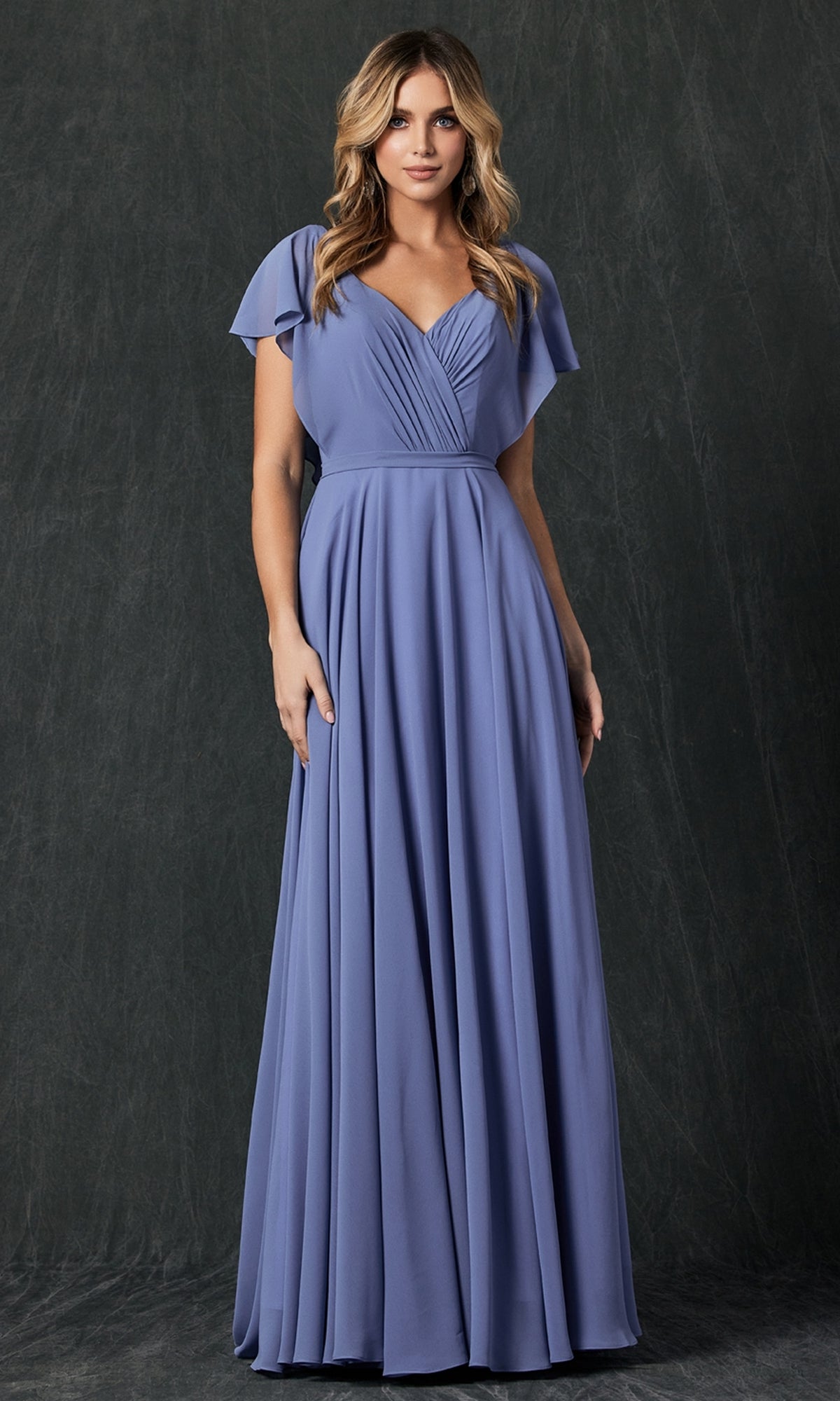 A woman stands against a dark background wearing the Flutter-Sleeve Long Formal Evening Gown 261—a floor-length, short-sleeved, light purple A-line dress with a pleated bodice and flowing skirt.